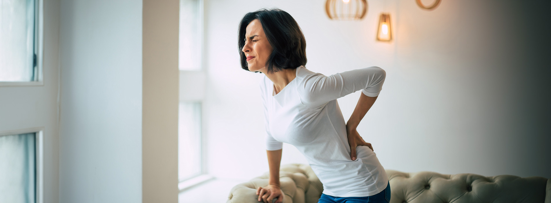The image depicts a person standing with their back to the camera, wearing a white top, and looking out of a window.