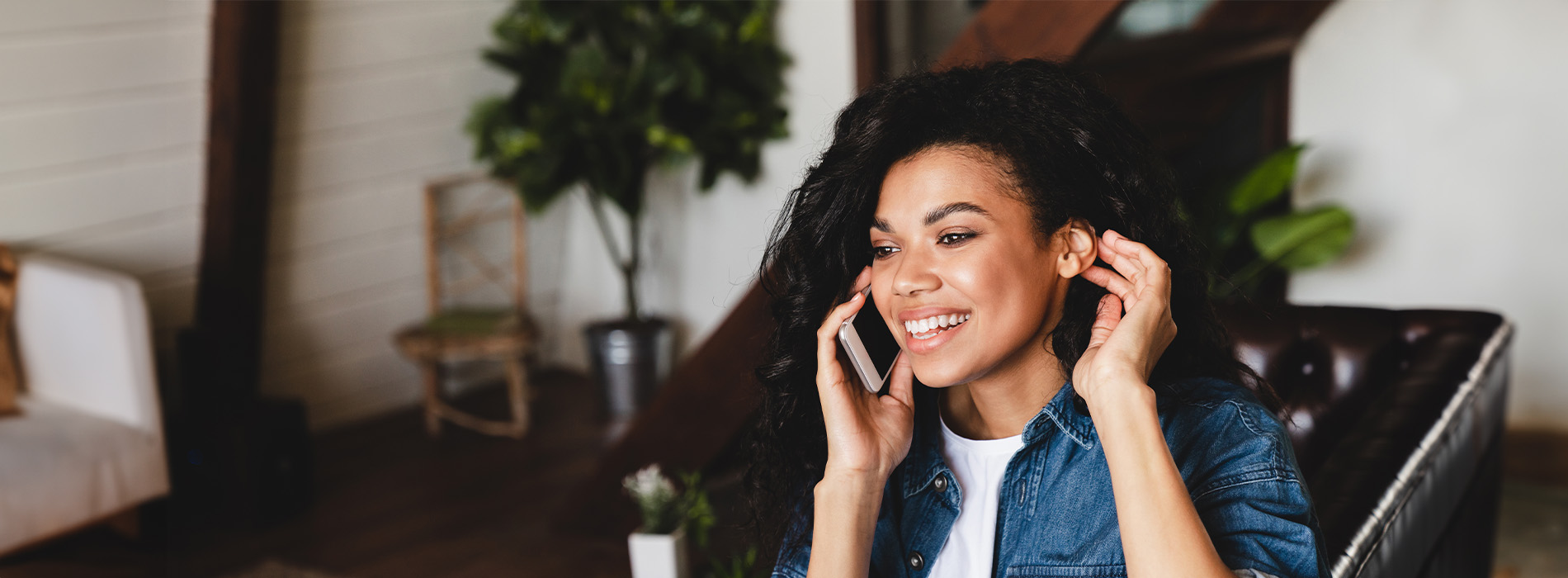 The image shows a person sitting at a desk with their hands on their head, smiling while talking on a phone.